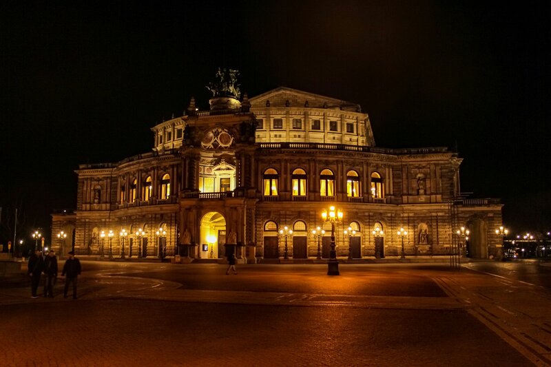 a large building lit up at night with people walking around