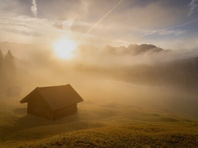 Geroldsee: A stunning sunrise emerging through the mist, with soft, golden light breaking through the fog in the foreground. The early morning haze creates a mystical atmosphere, as the sun rises above the horizon, casting a warm glow over the landscape. The peacefu