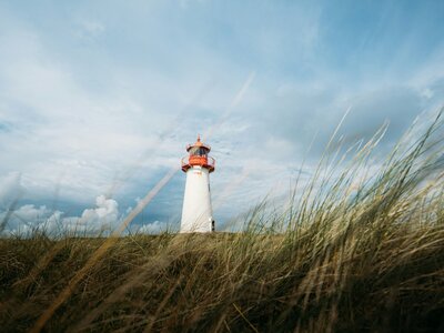 List-West Lighthouse Sylt: White lighthouse on grassy hill under dramatic cloudy sky.